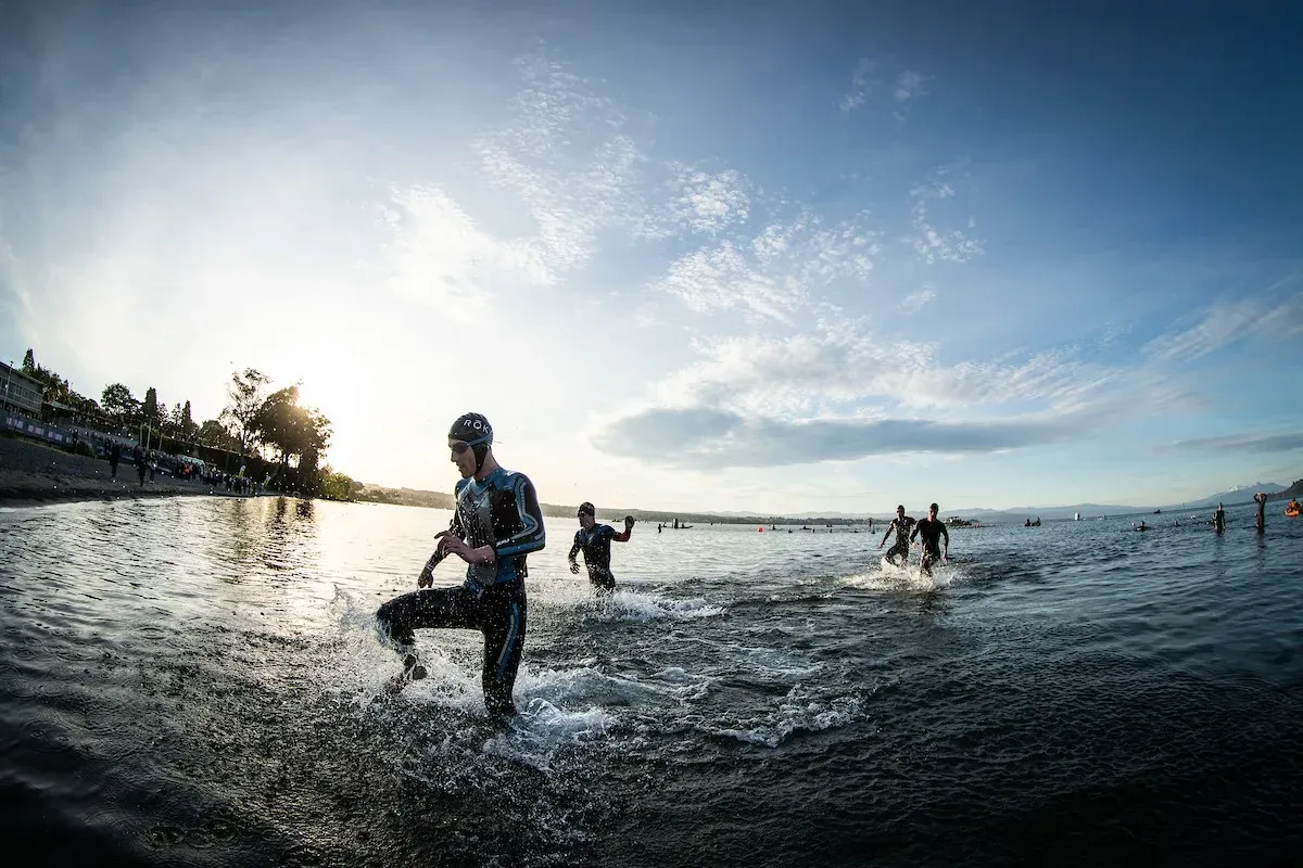 Triathletes running out of a lake at the start of a race, low sun behind them