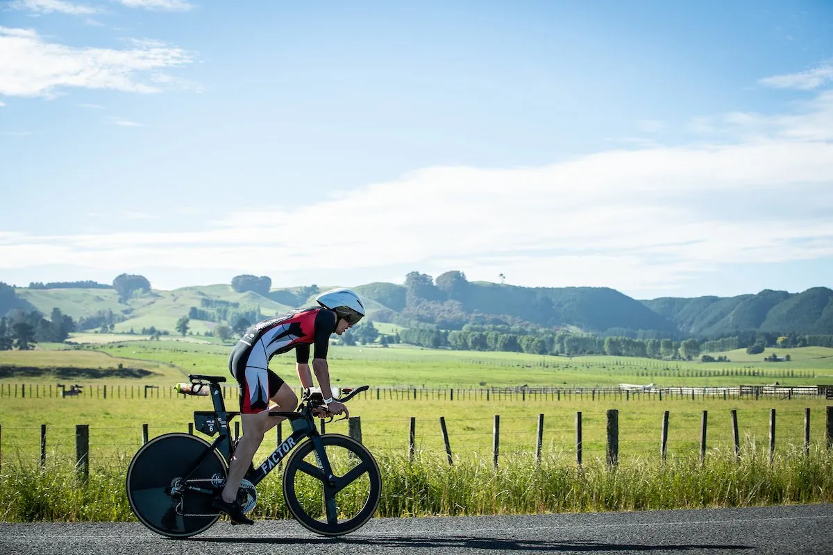 A triathlete on a time trial bike riding past farmland