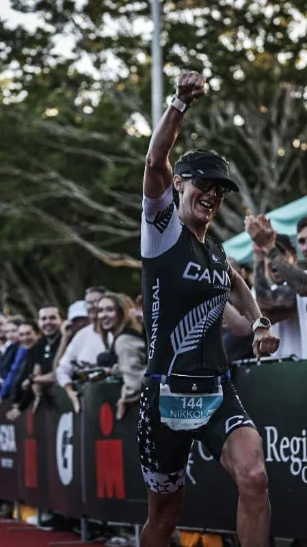 An athlete celebrating at a finish line, arms raised, crowd behind