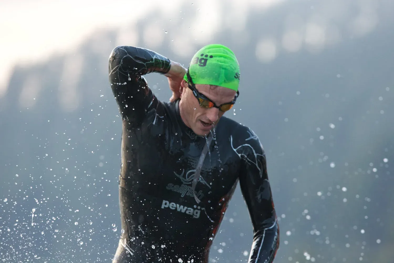 A triathlete in a wetsuit and green cap running out of the water